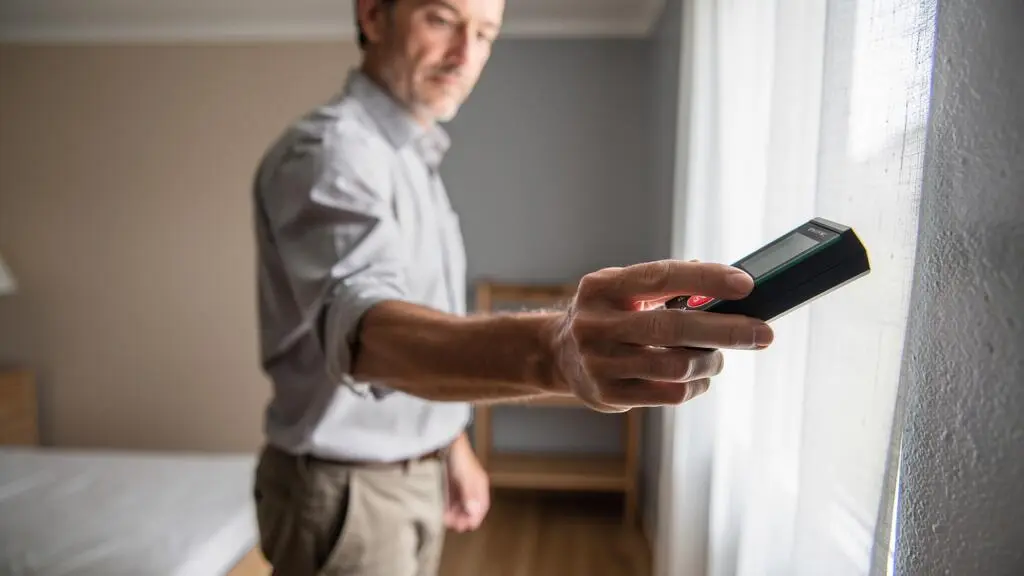 Une agente immobilière mesure une pièce avec un télémètre laser lors d'une visite d'estimation.