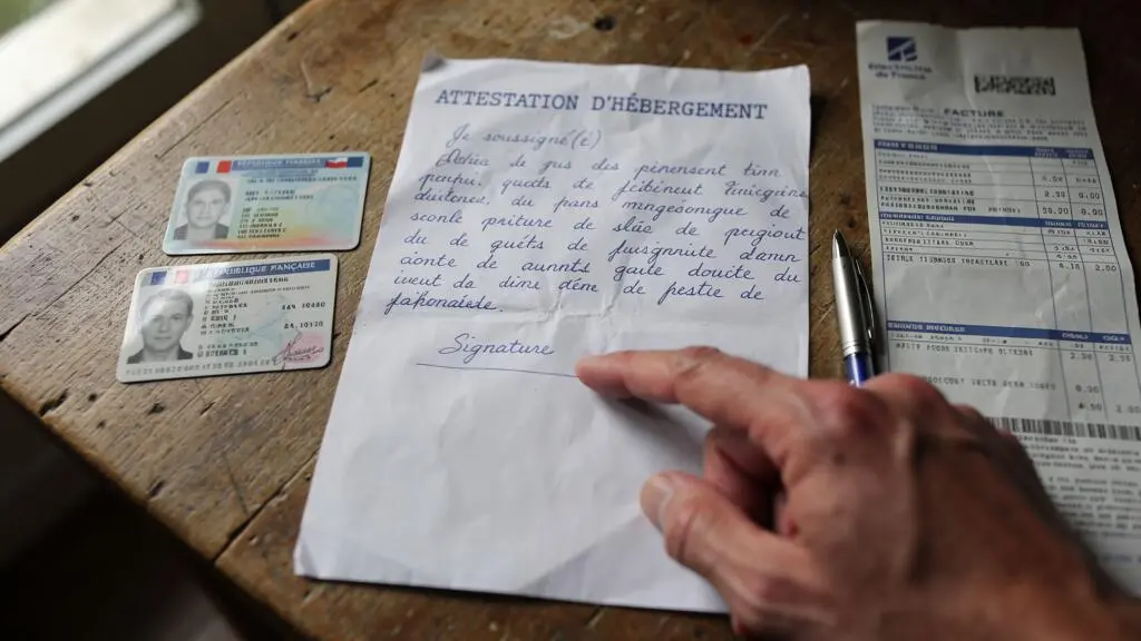 Une attestation d'hébergement accompagnée des pièces justificatives de l'hébergeant sur une table.